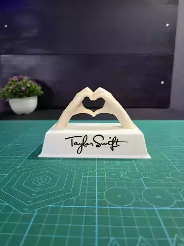 Taylor Swift base con dos manos formando un corazon