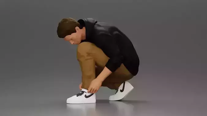 Man in hoodie crouching down tying shoelaces focused